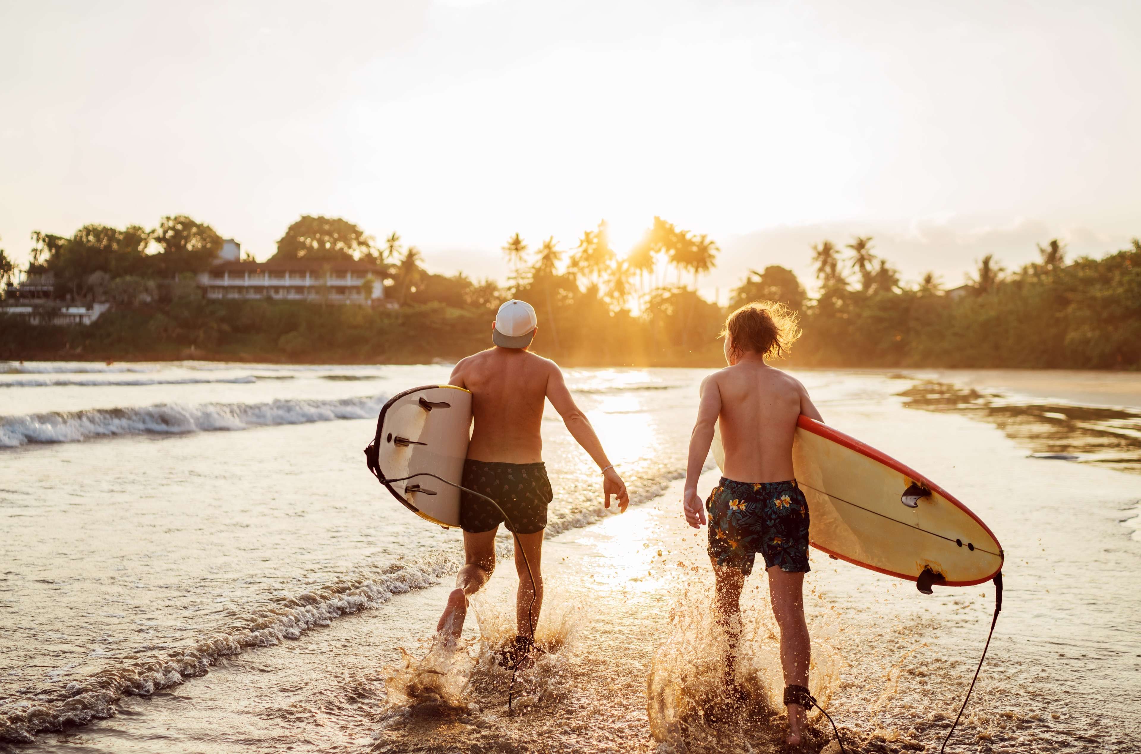 Two surfers walking down to the water at sunset
